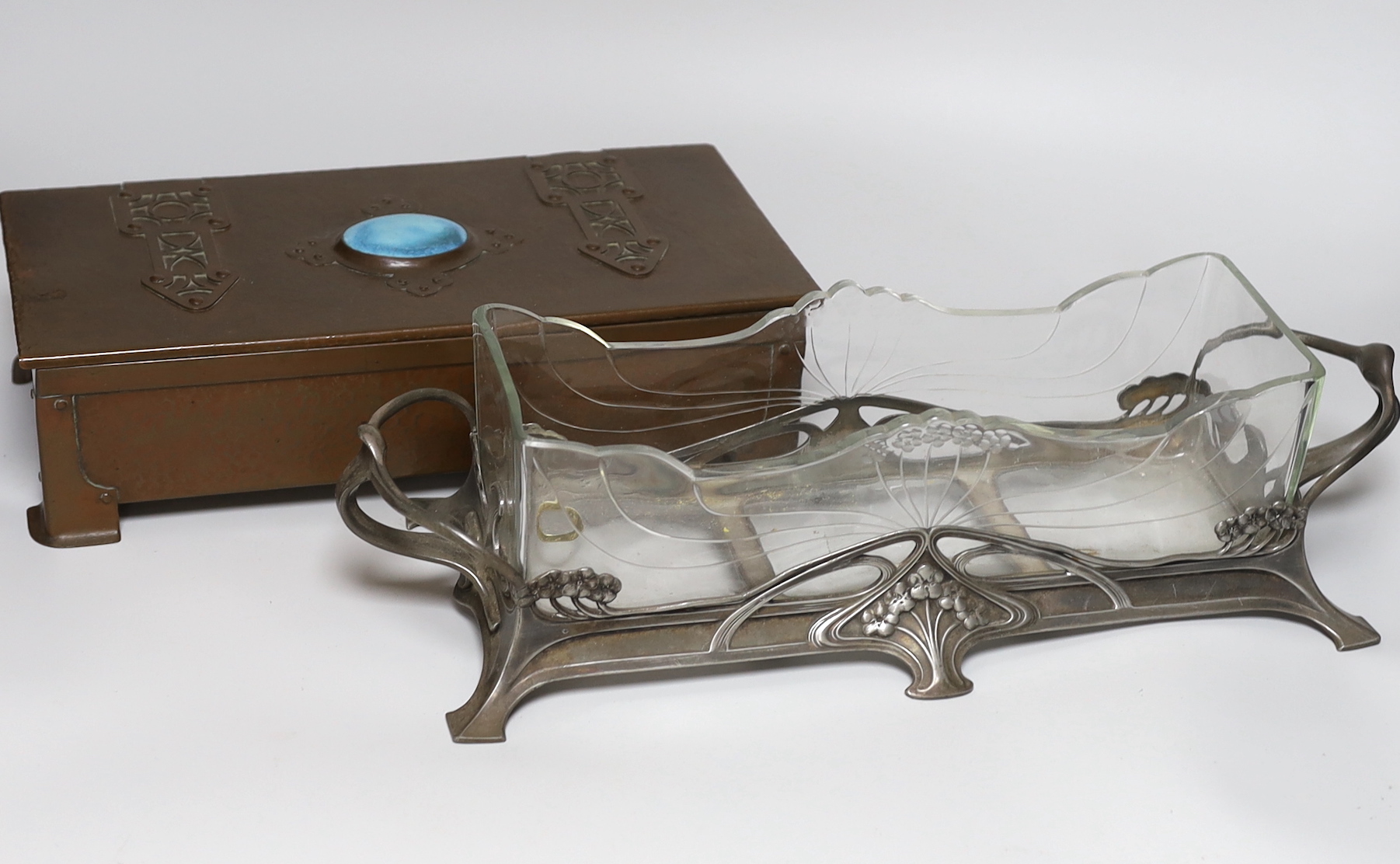 An Arts and Crafts copper box, the lid inset with a Ruskin porcelain plaque and an Art Nouveau pewter mounted glass centrepiece dish, 41 cm wide